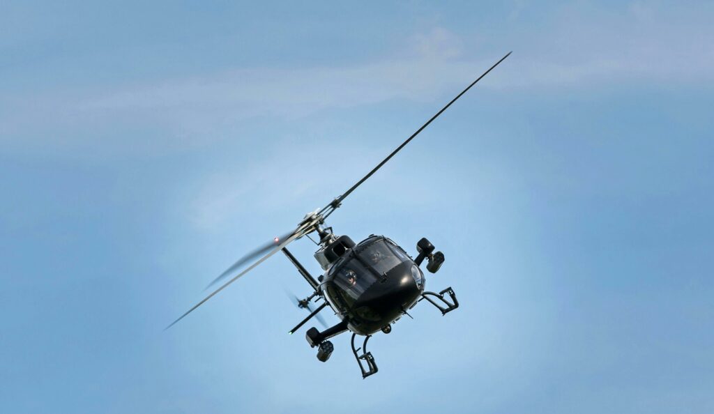 A black helicopter captured mid-flight in a clear blue sky, showcasing its dynamic presence and motion.